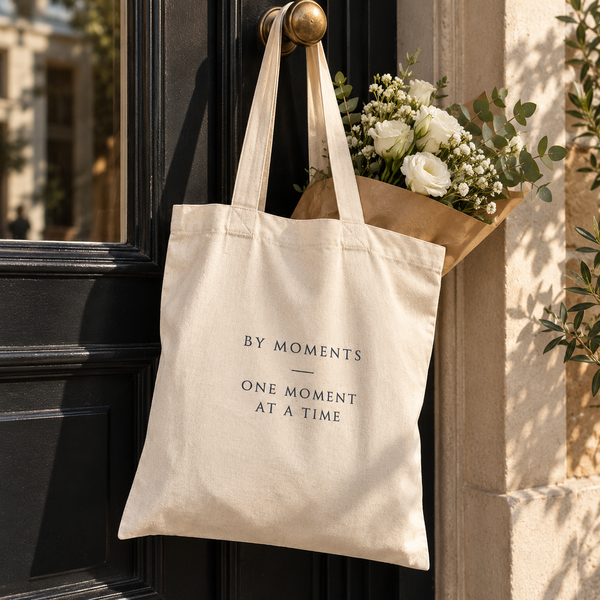By Moments Tote Bag hængende i rolige, varme omgivelser med blomster